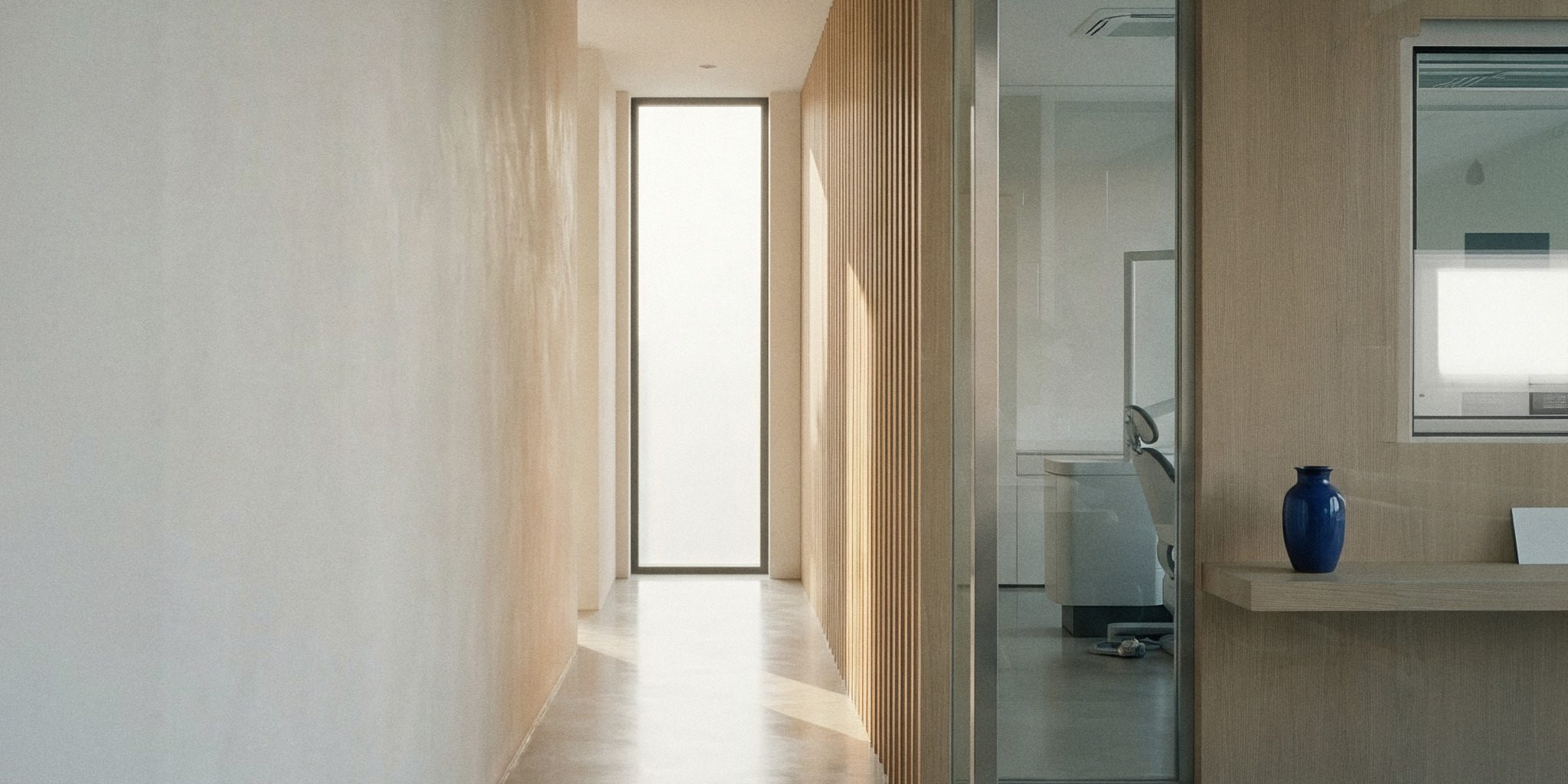 Corredor de uma clínica de odontologia com sala de atendimento atrás de uma divisória de vidro